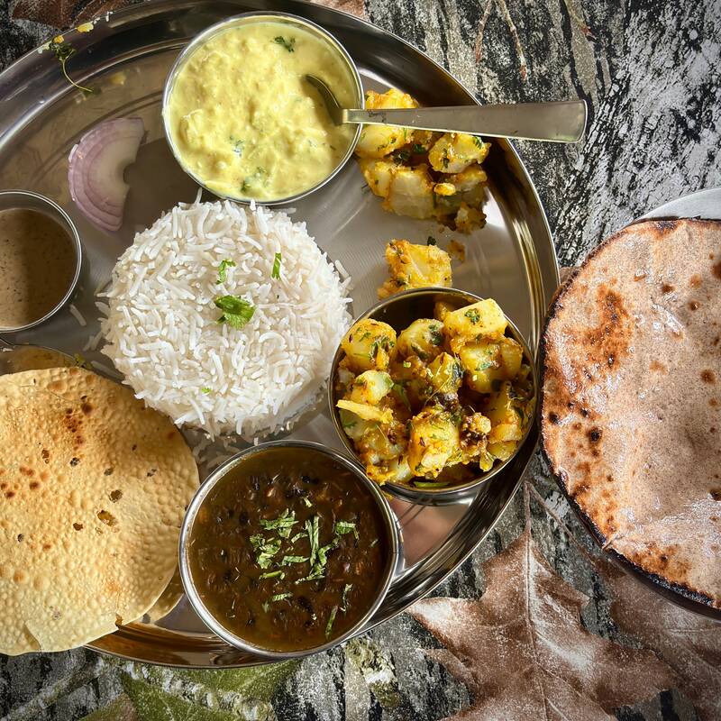 Home lunch thali with rice, roti, papad, dal and aloo gobi